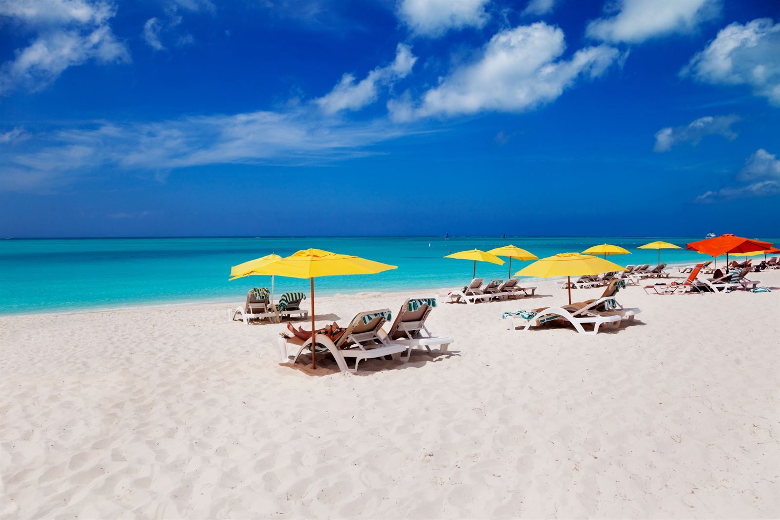 Yellow beach umbrellas and loungers on white sand by turquoise water in Turks and Caicos